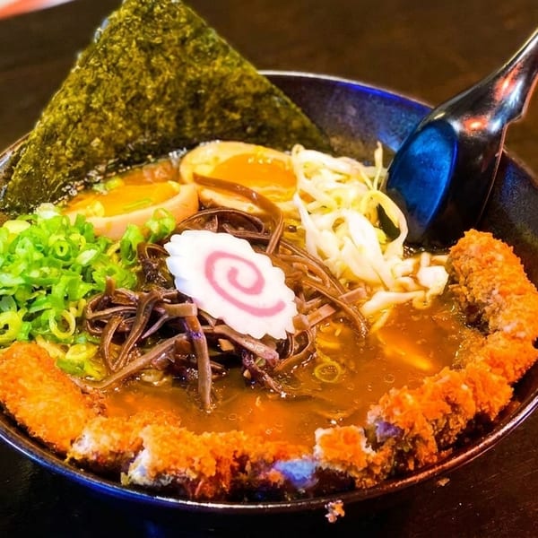 Close-up of a ramen bowl with broth, noodles, egg, seaweed, scallions, and fried cutlets.