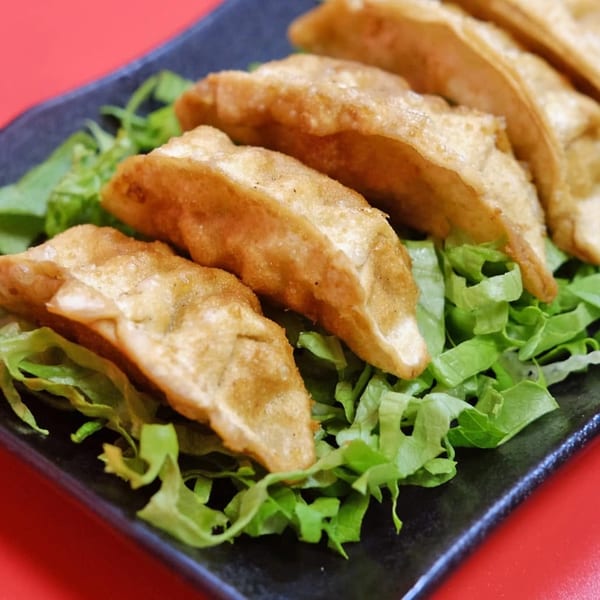 Golden-brown fried dumplings, or gyoza, arranged on a bed of fresh green lettuce on a black plate.