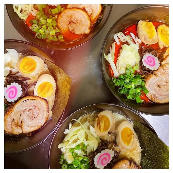 Four bowls of ramen with pork, eggs, green onions, and narutomaki on a metal surface.