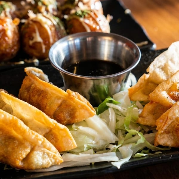 Crispy fried gyoza with a side of shredded cabbage and a dipping sauce, with takoyaki in the background.