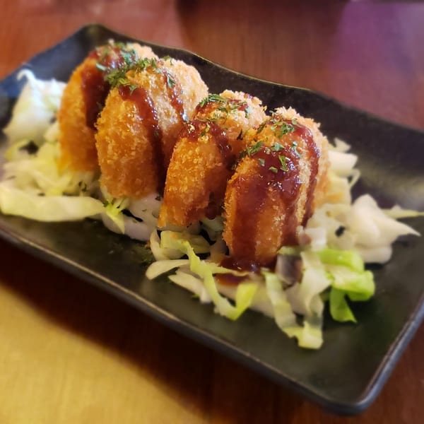 Four golden-brown fried croquettes drizzled with sauce and garnished with parsley, served on shredded cabbage.
