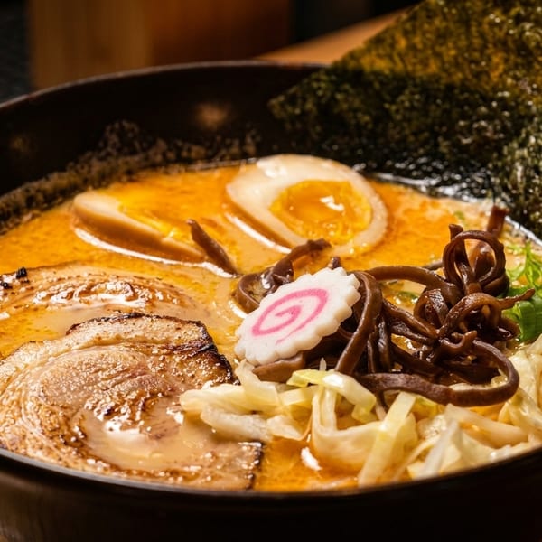 A close-up of a bowl of ramen with pork, egg, narutomaki, seaweed, and green onions.