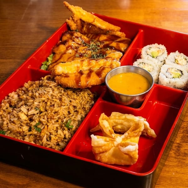A bento box with fried rice, sushi rolls, fried chicken, and a dipping sauce.